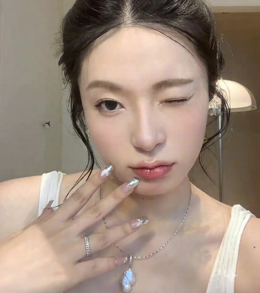 Gros plan dune main aux ongles de style chrome argenté tenue près du visage avec une expression clin dœil.