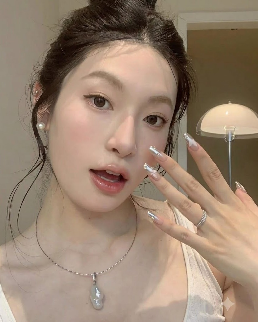 Un plan rapproché stable dune main levée vers la joue mettant en valeur des ongles chrome argenté avec des accents papillon.