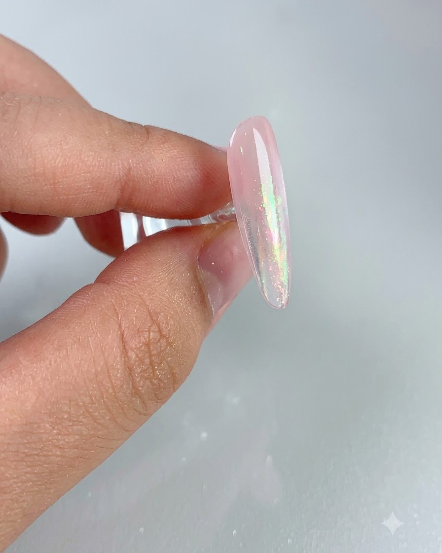 Gros plan sur un ongle rose brillant révélant un effet aurora scintillant après avoir balayé lexcédent de poudre.
