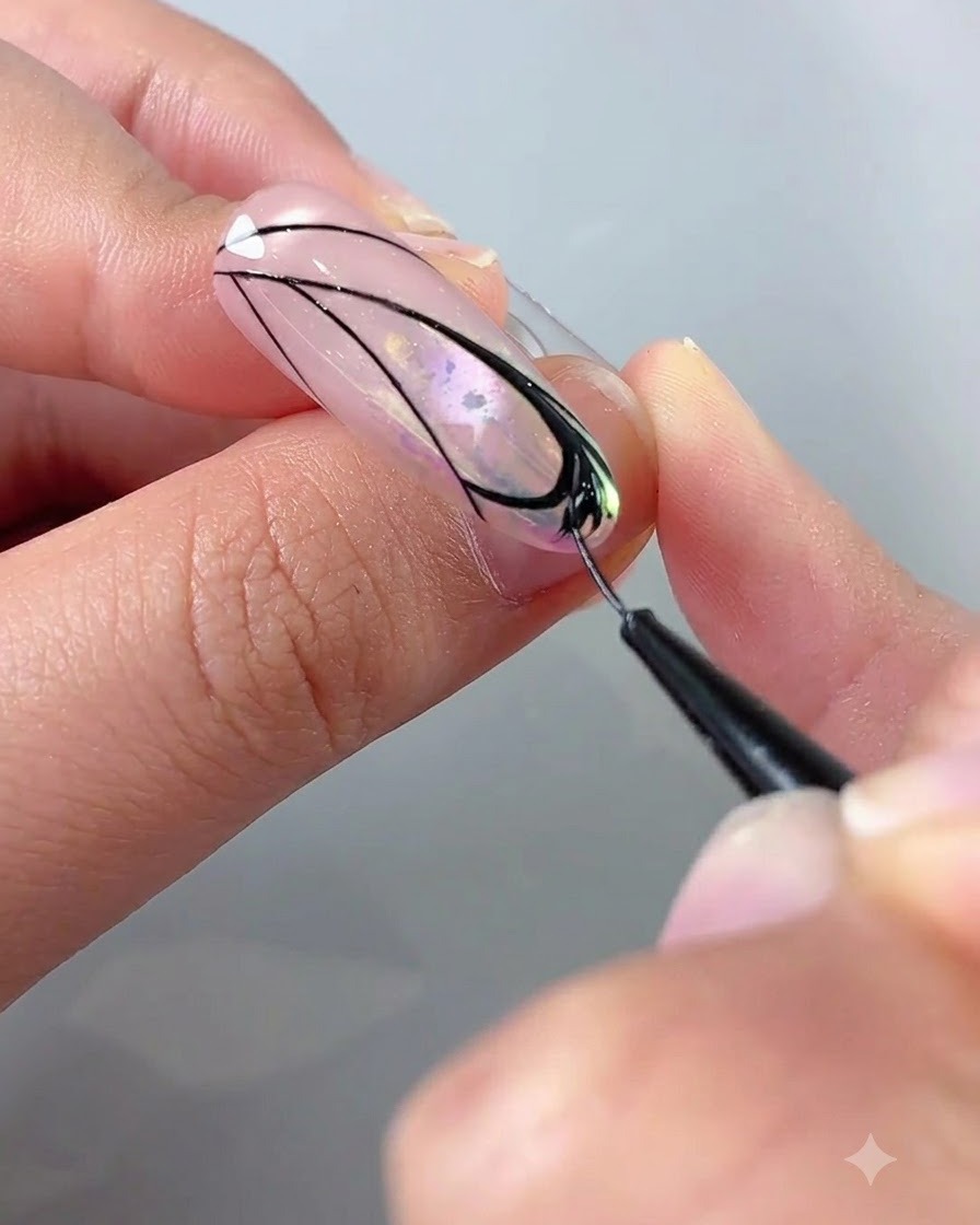Gros plan sur une main utilisant un pinceau fin avec du gel noir pour remplir les détails à lintérieur dun motif daile de papillon sur un ongle.
