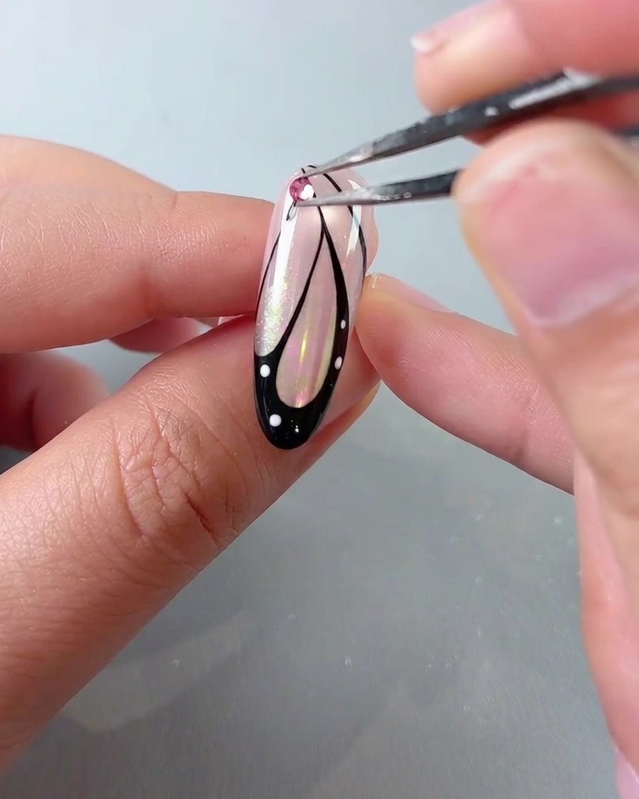 Une paire de pinces plaçant un strass en cristal rose sur le haut dun design dongle daile de papillon.