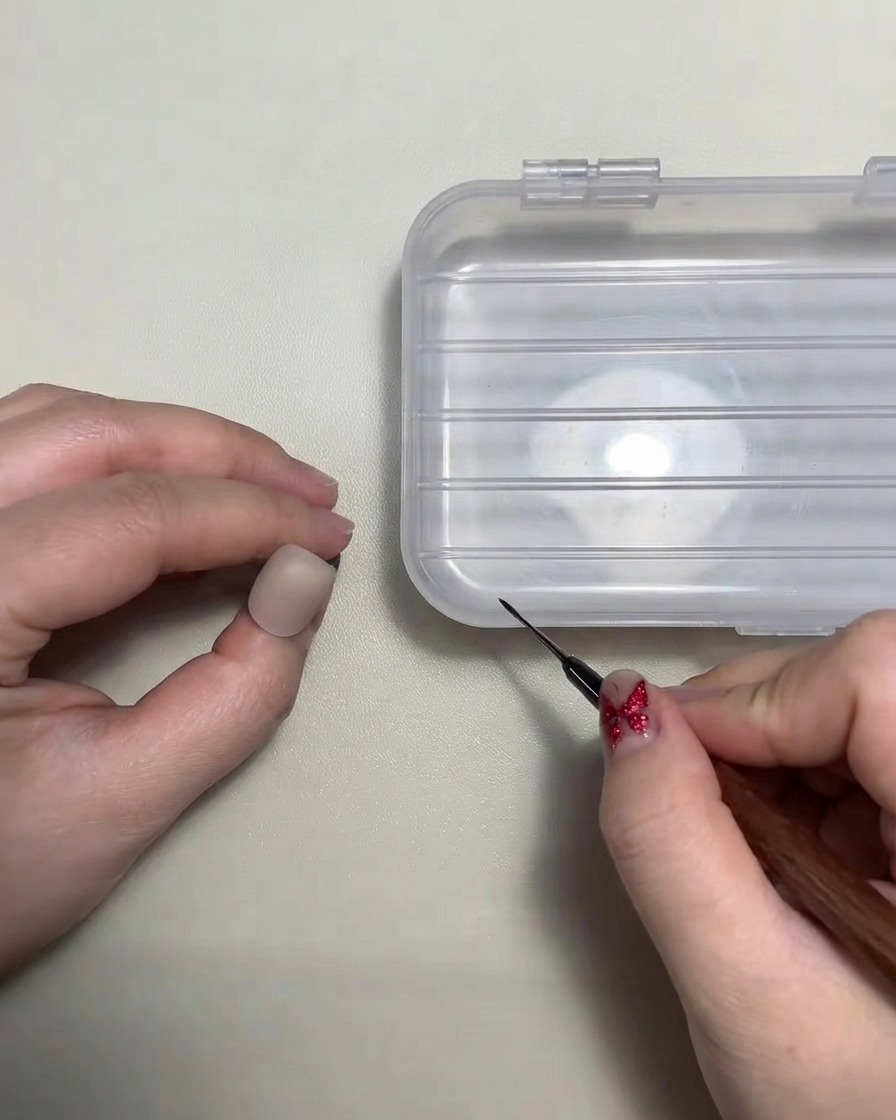 Une prothésiste ongulaire tenant un pinceau liner fin près dun faux ongle dentraînement.