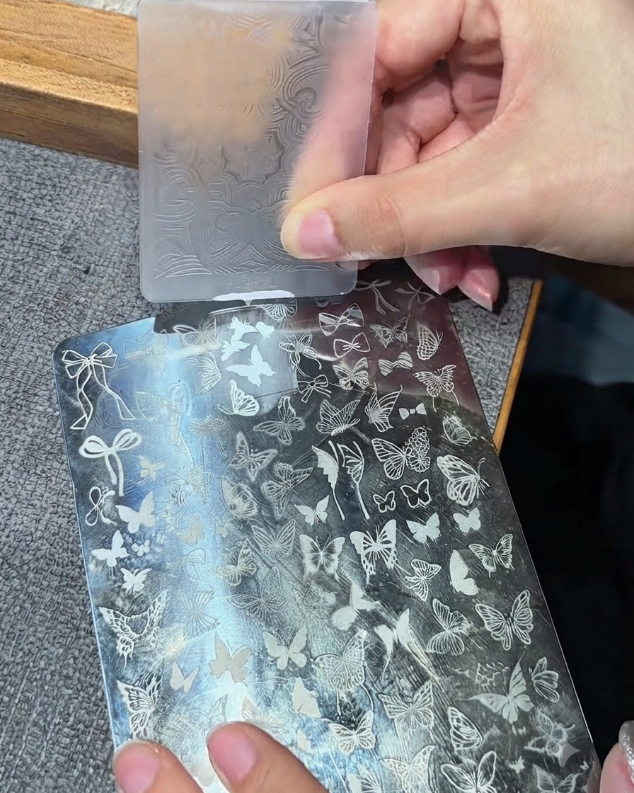 Une tête de tampon en silicone transparent appuyant sur une plaque de stamping métallique pour prélever un motif blanc.