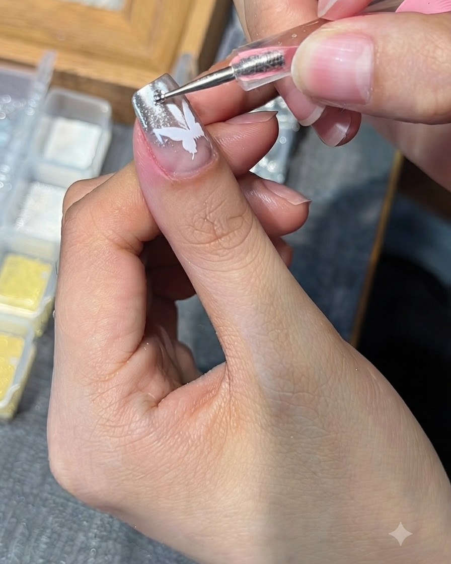 Un outil de dotting plaquant un petit strass sur un ongle orné dun motif de papillon blanc.