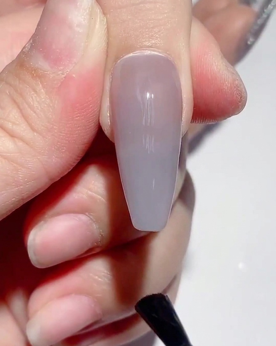 Pinceau appliquant une couche uniforme de top coat mat sur un ongle verni.