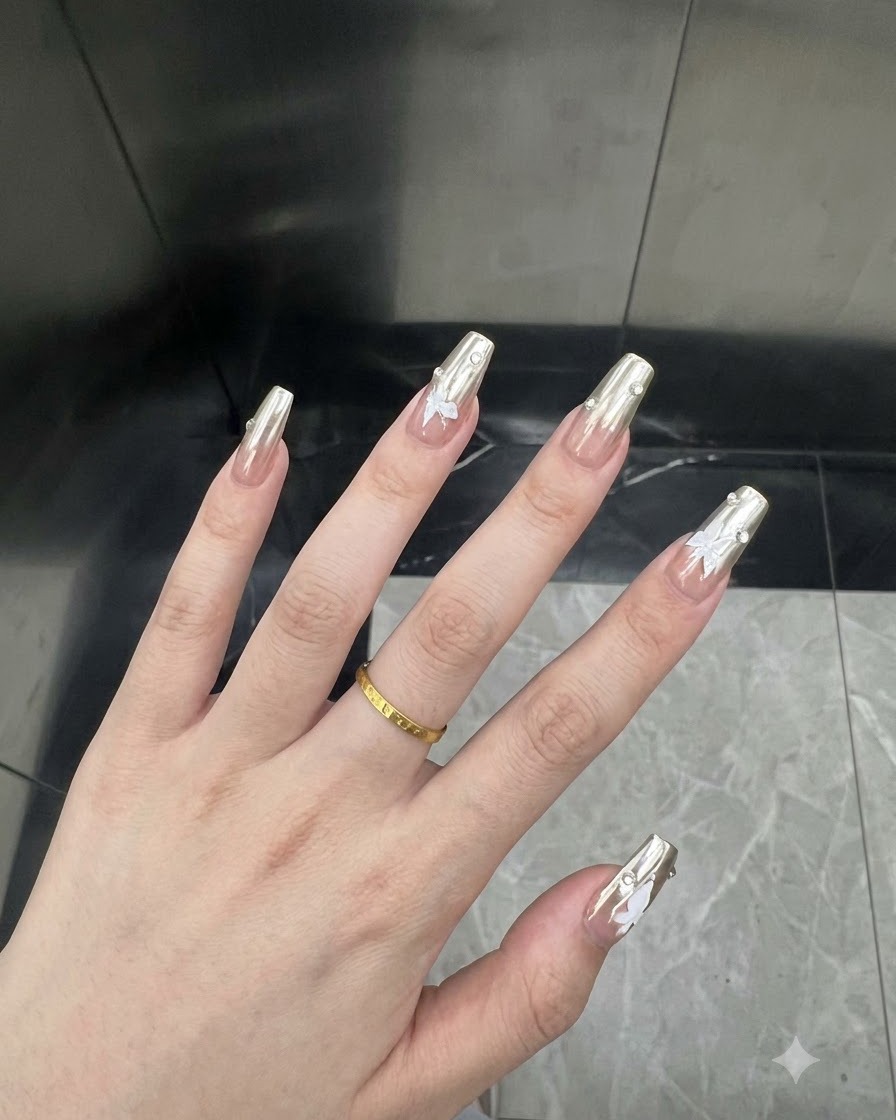 Gros plan macro dun ongle de pouce présentant un vernis chrome argenté et un petit autocollant papillon blanc.