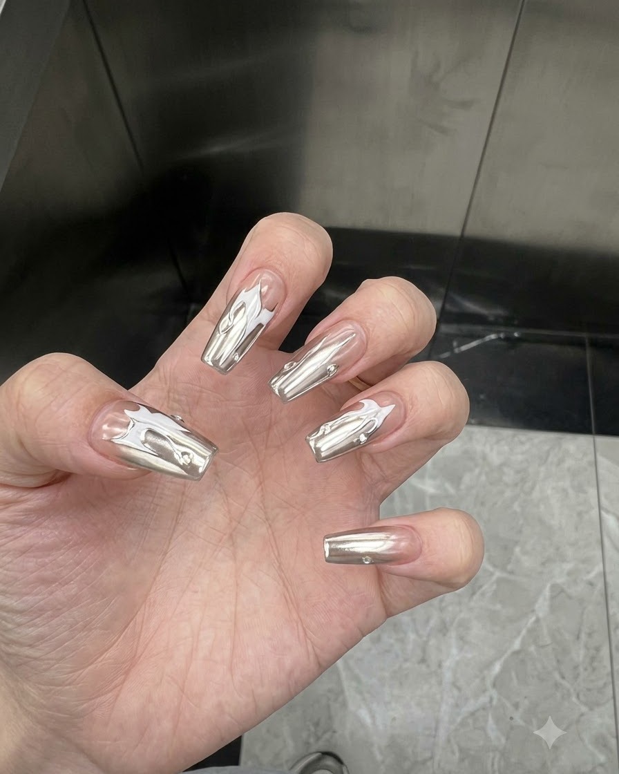 Main inclinée pour montrer la finition miroir réfléchissante des ongles enduits de chrome argenté sous un éclairage intérieur.