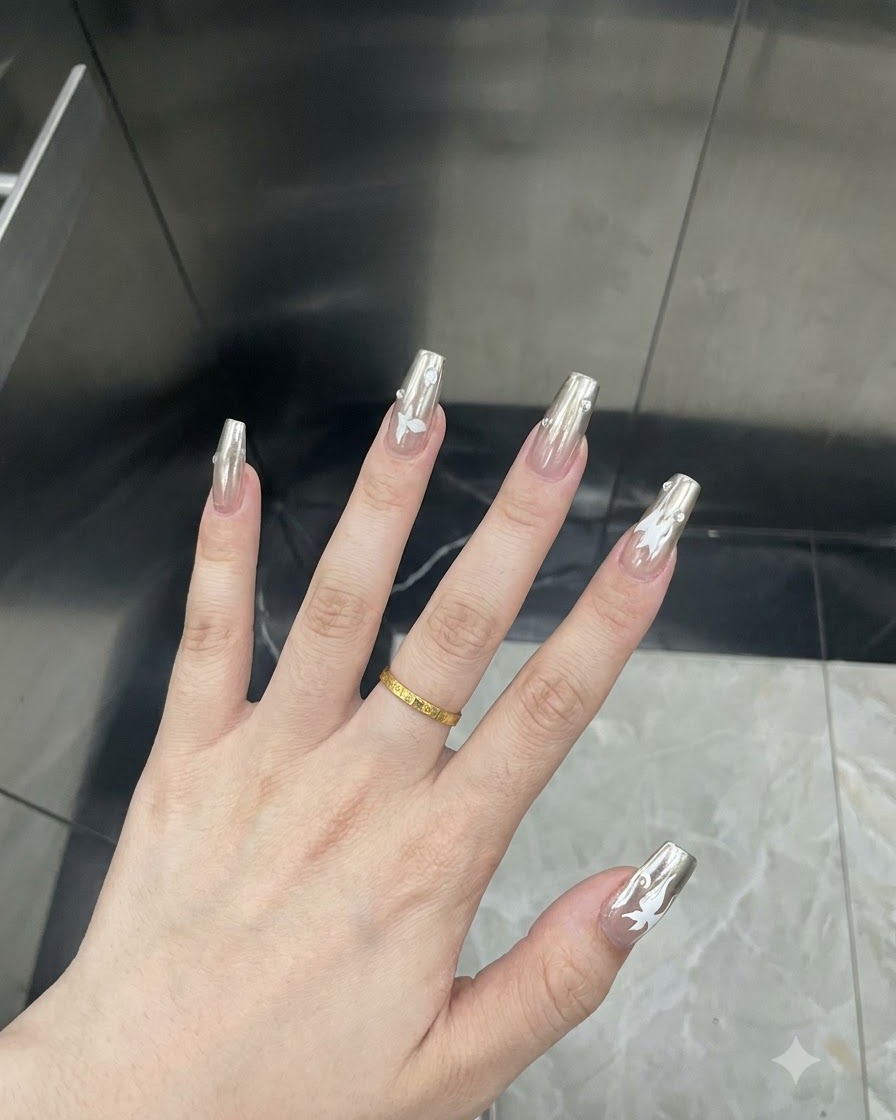 Gros plan détaillé dun doigt montrant un décalcomanie de papillon blanc appliqué sur un ongle en chrome argenté.