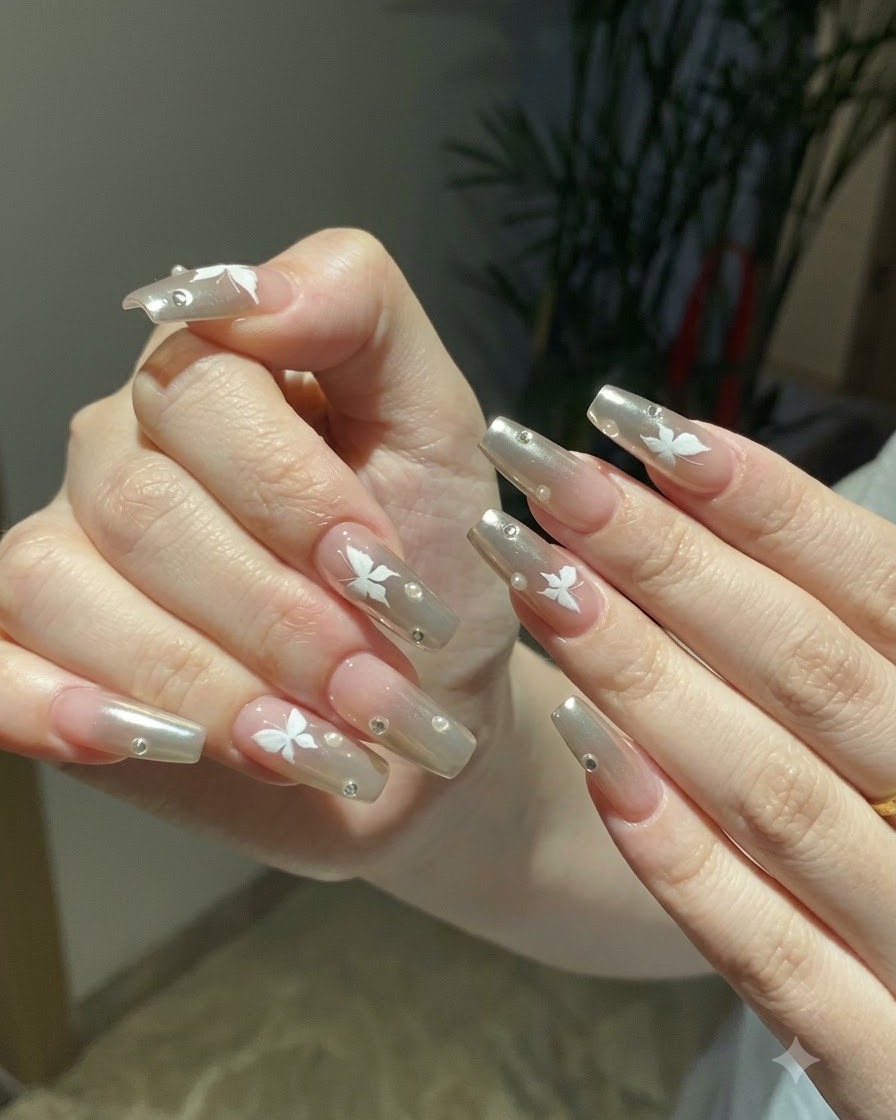 Deux mains posées ensemble affichant le nail art complet chrome argenté et papillon sous un éclairage intérieur chaleureux.