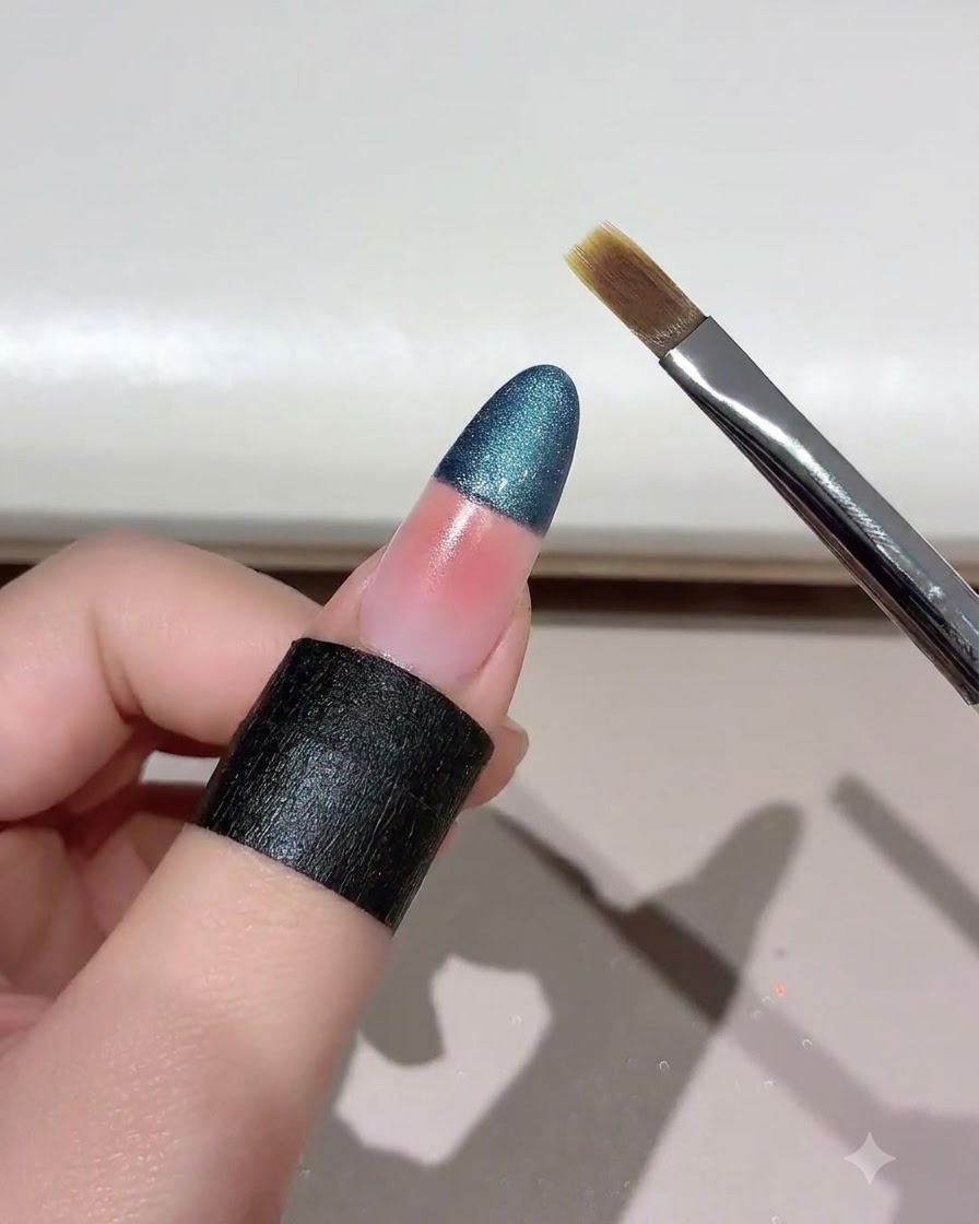 Un pinceau à ongles tenu en biais près dun ongle œil de chat estompé en dégradé.