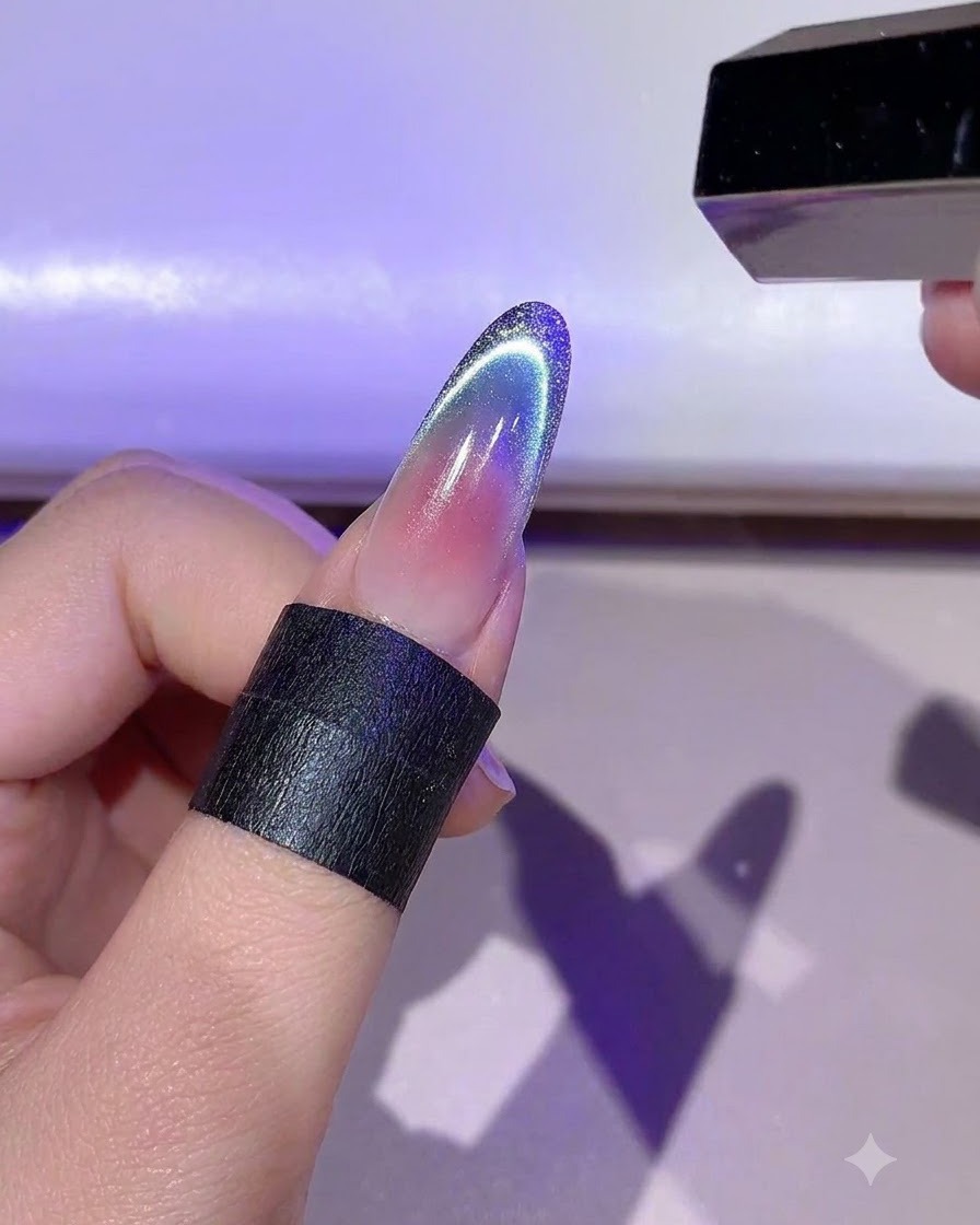 Une main tenant une mini lampe LED qui catalyse le contour détaillé en gel doré sur un ongle.