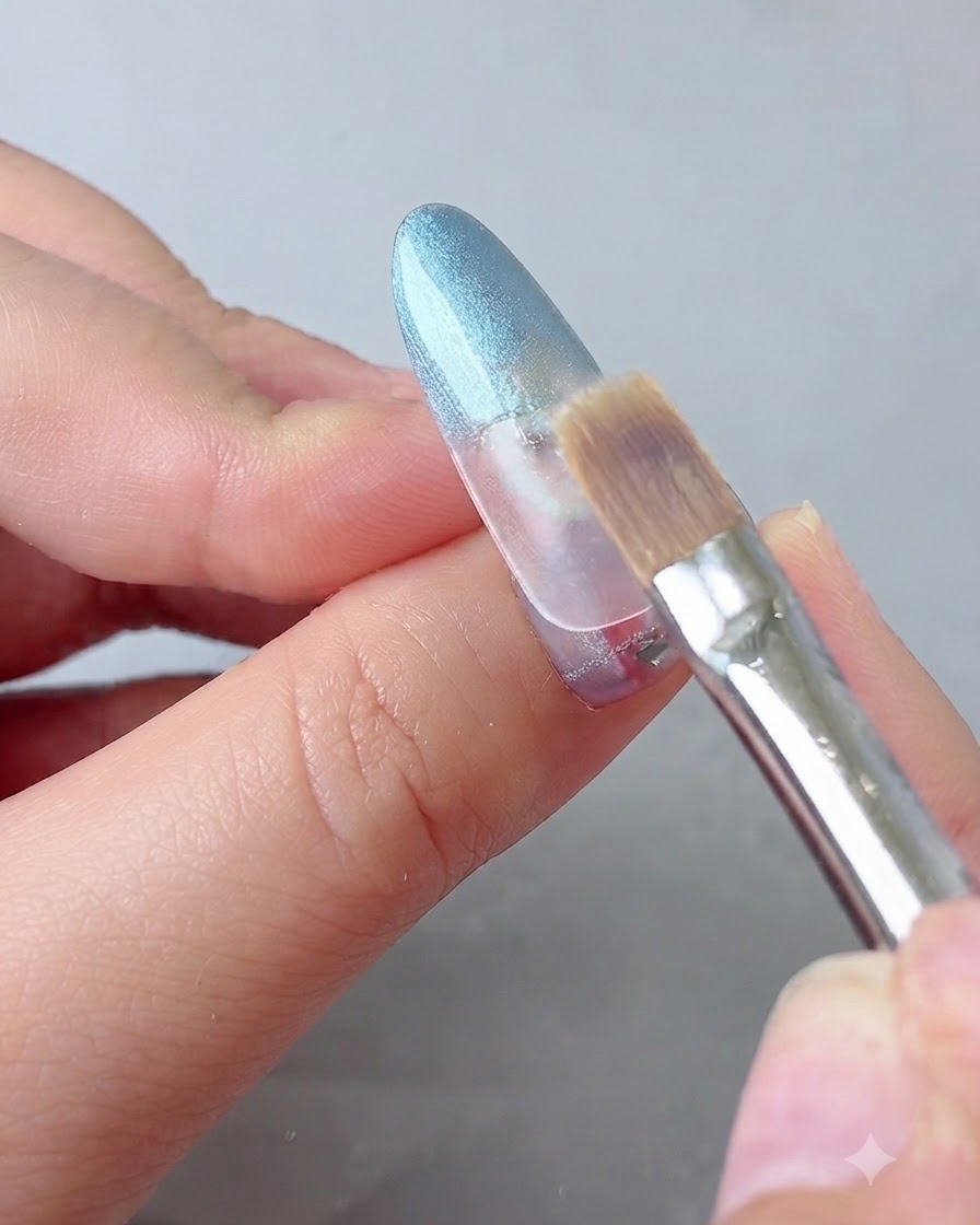 Un pinceau destompage adoucissant délicatement la transition du gel bleu sur un ongle.