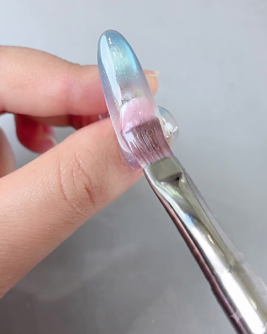 Un pinceau appliquant du gel rose sur la partie arrière de longle.