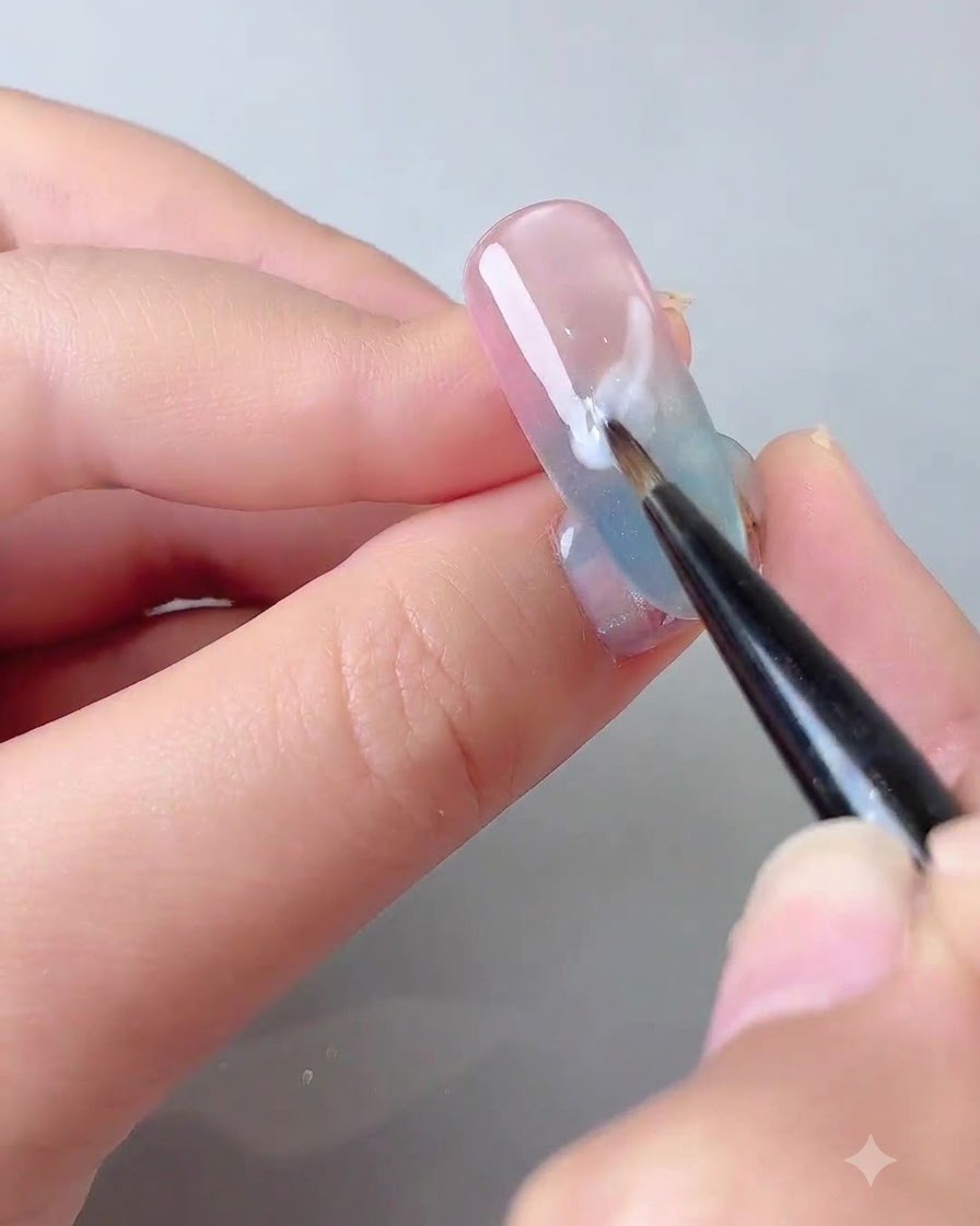 Un pinceau fin de détail appliquant un gel blanc auto-égalisant en forme de nuage doux sur un ongle en dégradé.