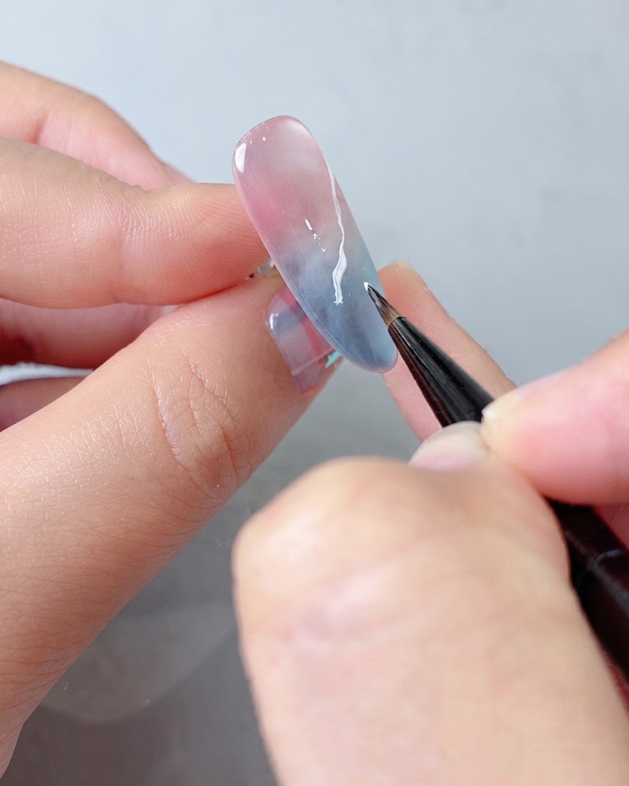Un pinceau de détail appliquant une couche supplémentaire de gel blanc sur le motif de nuage pour plus de profondeur.