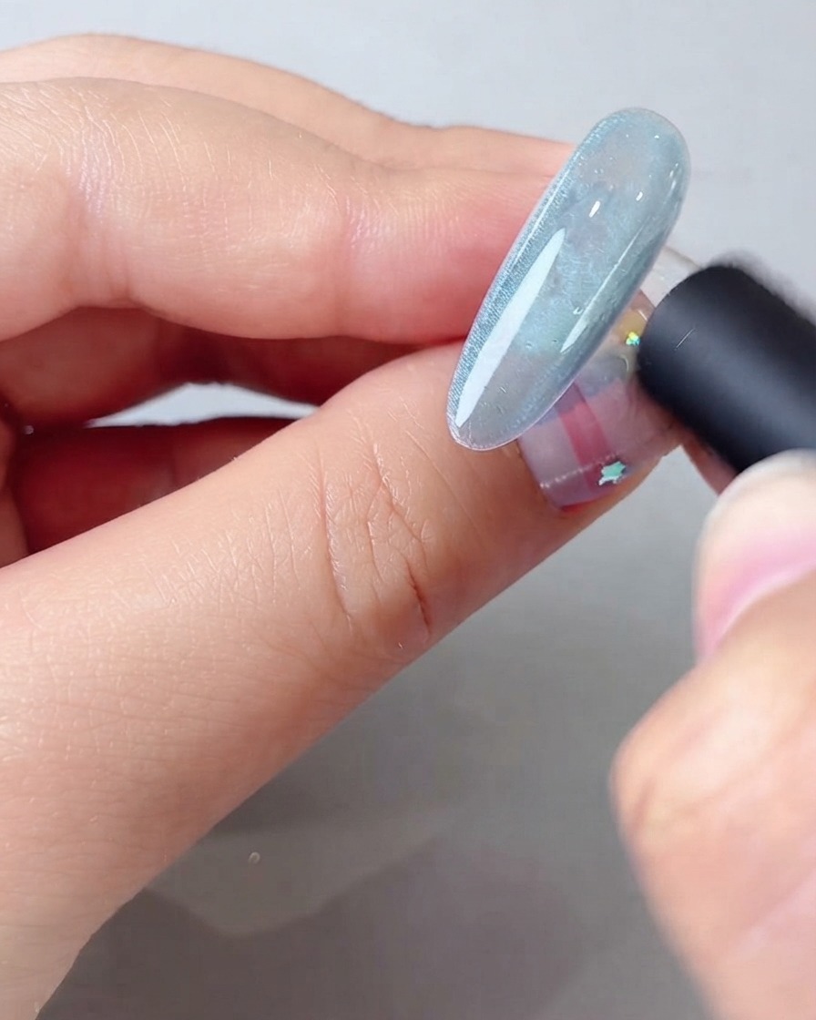 Un outil magnétique tenu près dun ongle en gel cat eye bleu pour former un large faisceau lumineux scintillant.