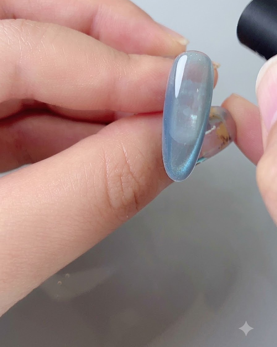 Un outil magnétique façonnant larc de reflet latéral sur un ongle en gel cat eye bleu.