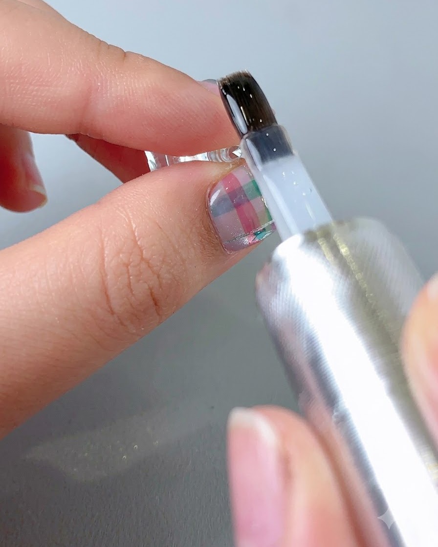 Un pinceau appliquant un top coat transparent et brillant sur la surface dun ongle à motifs fini.