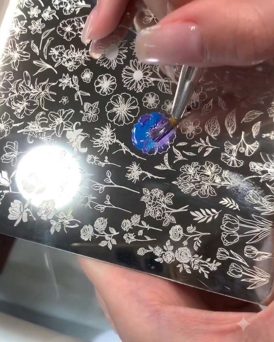 Une plaque destampage en acier avec un motif floral gravé où du gel bleu et violet est mélangé avec un pinceau.