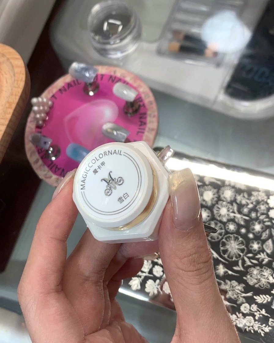 Une main tenant un produit destampage blanc en flou avec des caractères asiatiques et une plaque destampage à ongles en arrière-plan.