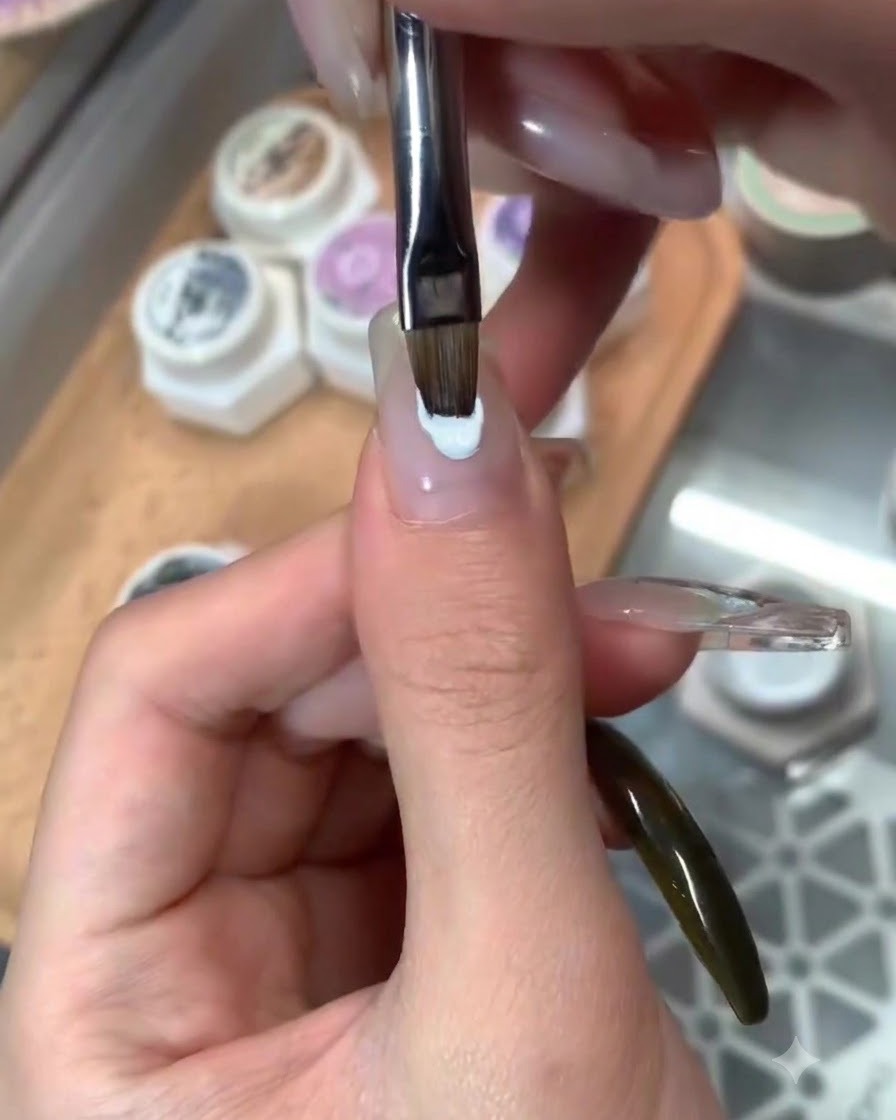 Un pinceau appliquant une couche de finition brillante sur un nail art à thème bleu terminé.