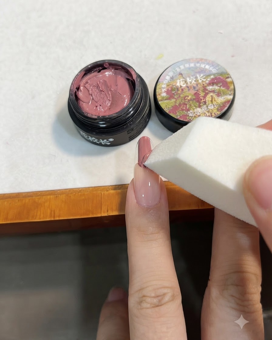 Une éponge de maquillage blanche tapotant le gel rose sur longle pour lestomper vers le bas en dégradé.