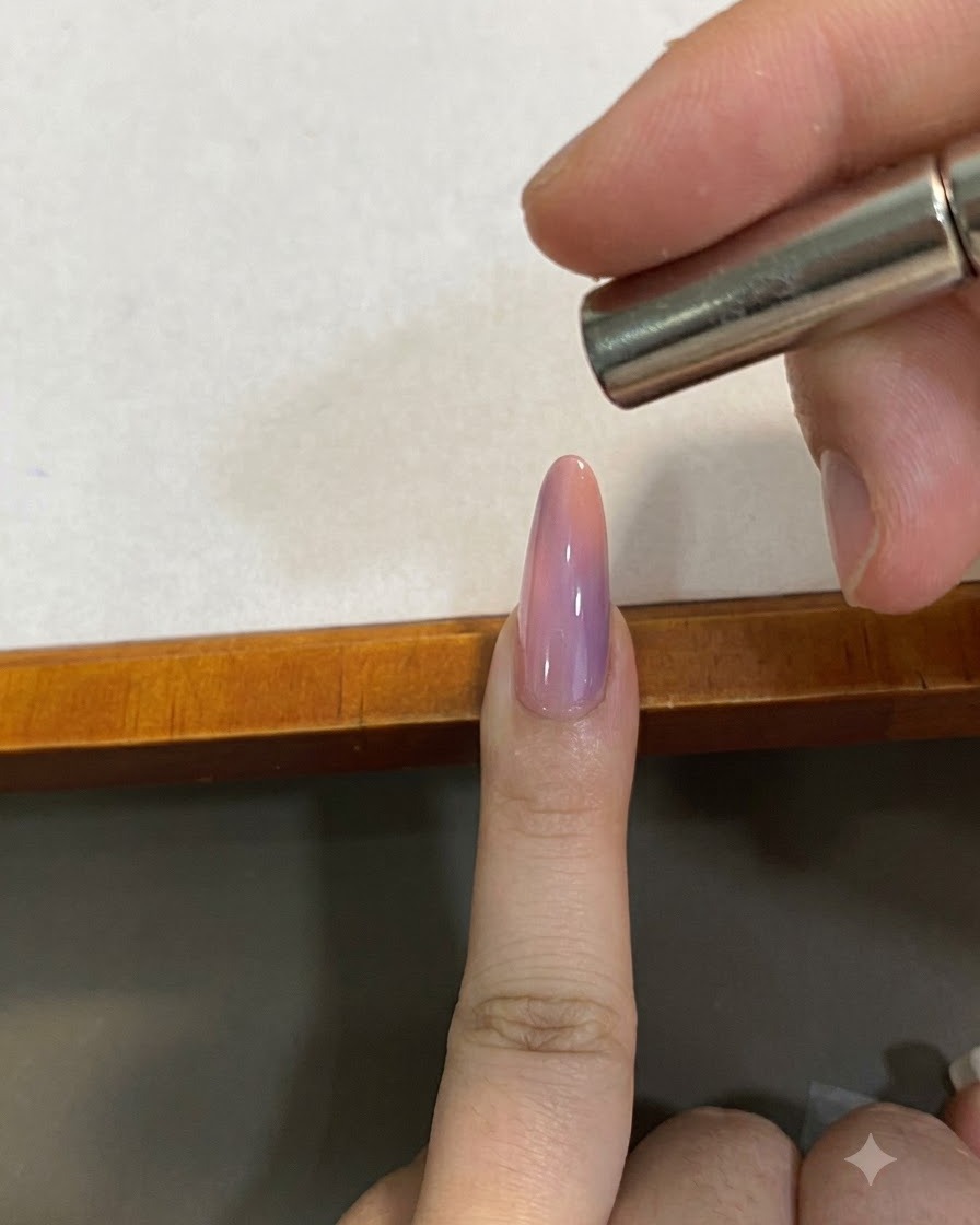 Un petit aimant tenu de près au-dessus dun ongle rose dégradé effet œil-de-chat pour façonner le pigment magnétique.