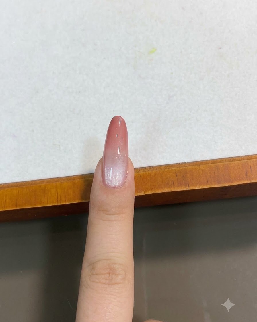 Un ongle rose pêche avec effet œil-de-chat dégradé terminé, vu en gros plan en plongée.