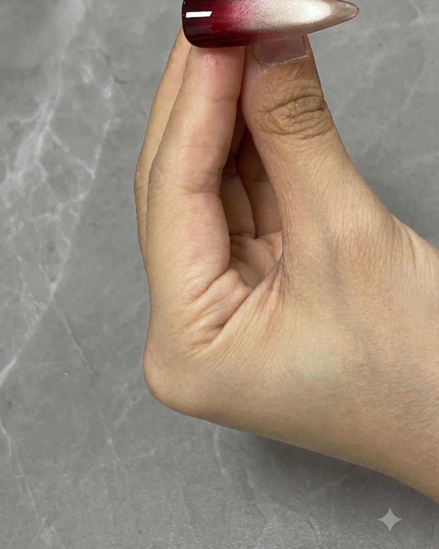Un pinceau de nail art appliquant du gel rouge translucide sur la moitié supérieure dun ongle décoré.