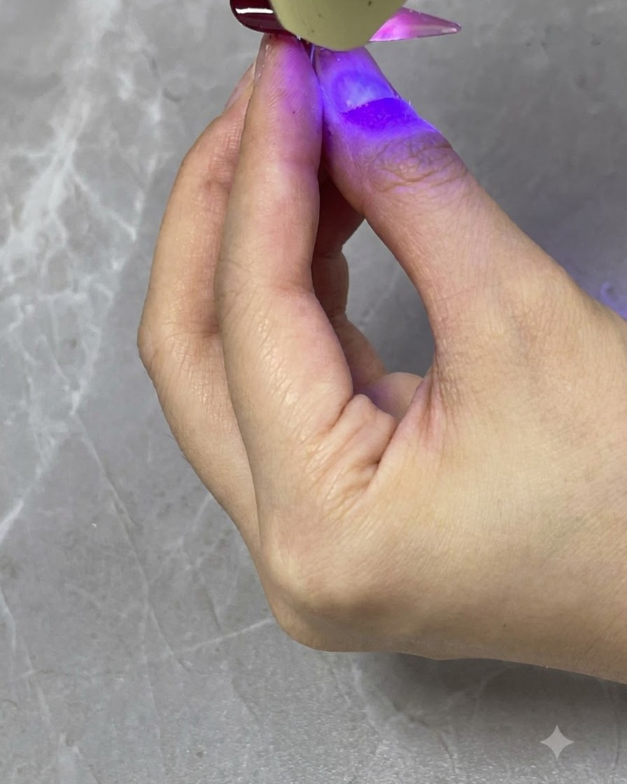 Une lampe UV LED portative catalysant une couche de dégradé rouge translucide sur un ongle fini.