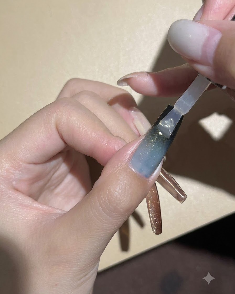 Un pinceau à ongle appliquant un top coat transparent brillant sur le dégradé sombre et longle en gel œil de chat.