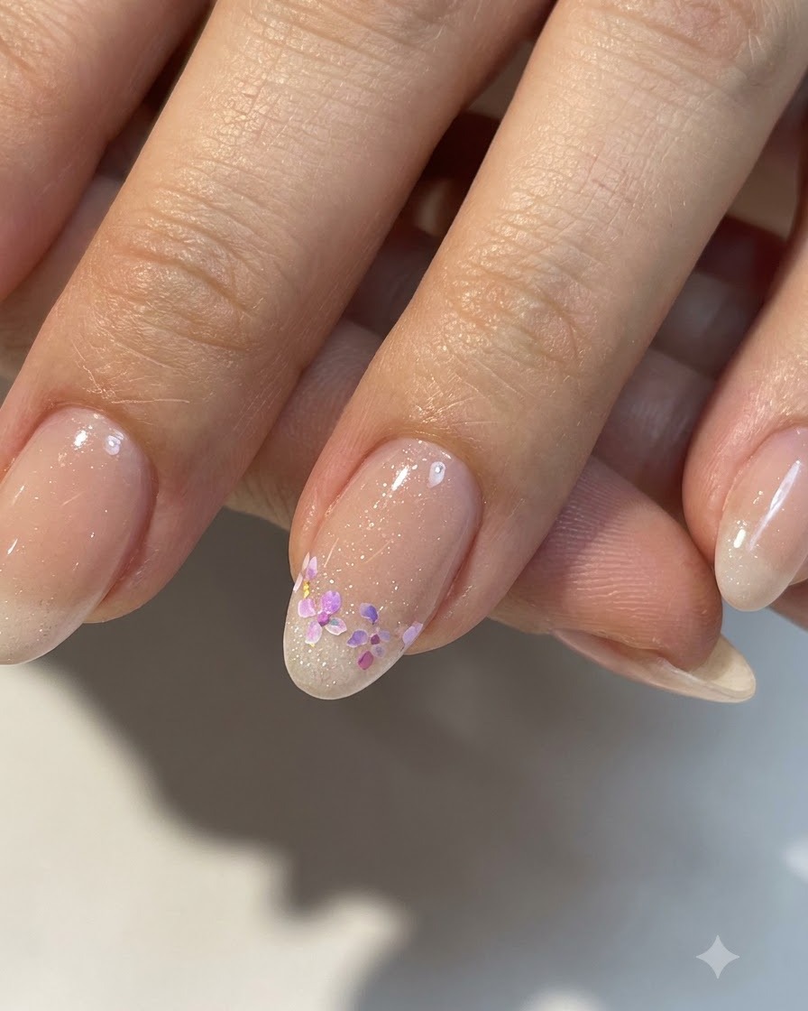 Un gros plan dun petit nail art floral terminé sur une base nude brillante avec des détails raffinés.