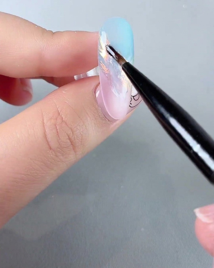 Un pinceau fin pour nail art appliquant des détails de paillettes iridescentes étincelantes sur un ongle dégradé pastel.
