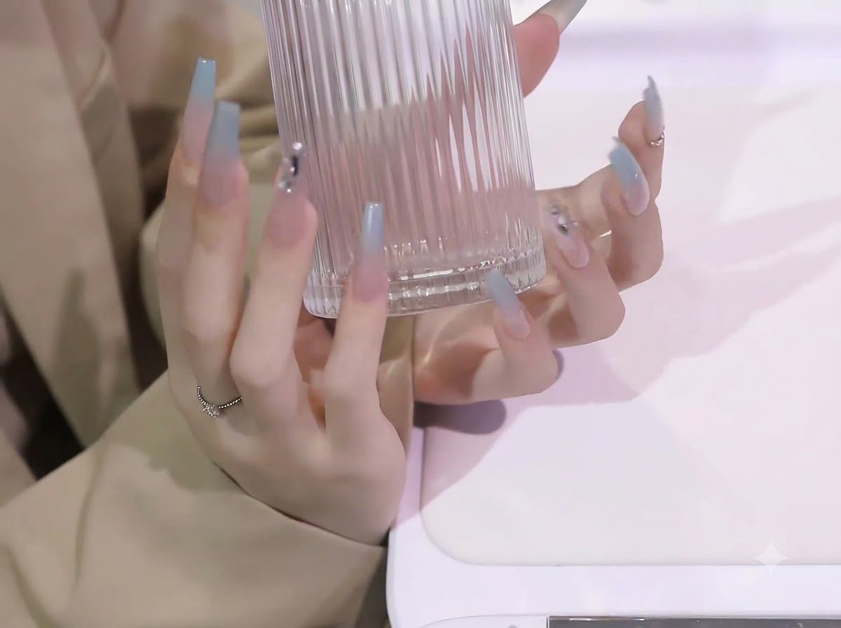 Les deux mains soulevant un récipient en verre transparent et côtelé, affichant la longueur et la courbure des extensions dongles dégradées en bleu.