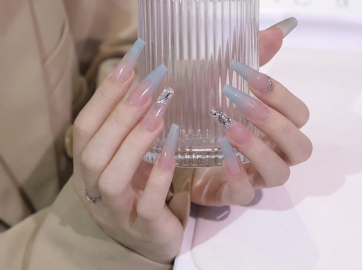 Mains ajustant leur prise sur un verre pour présenter la transition de dégradé fluide du bleu au nude sur des ongles coffin longs.