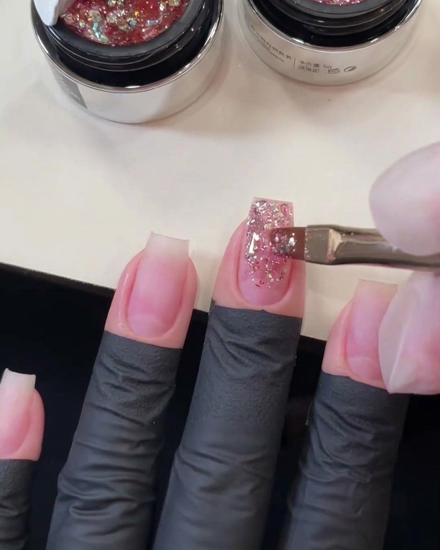 Pinceau à gel plat balayant les sequins roses épais le long de longle du majeur pour former un dégradé de paillettes.