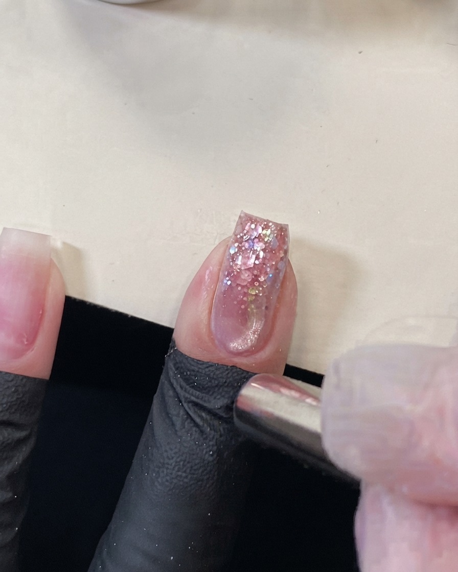 Aimant cylindrique tenu près de la pointe dun ongle à paillettes roses pour repousser leffet œil de chat magnétique.