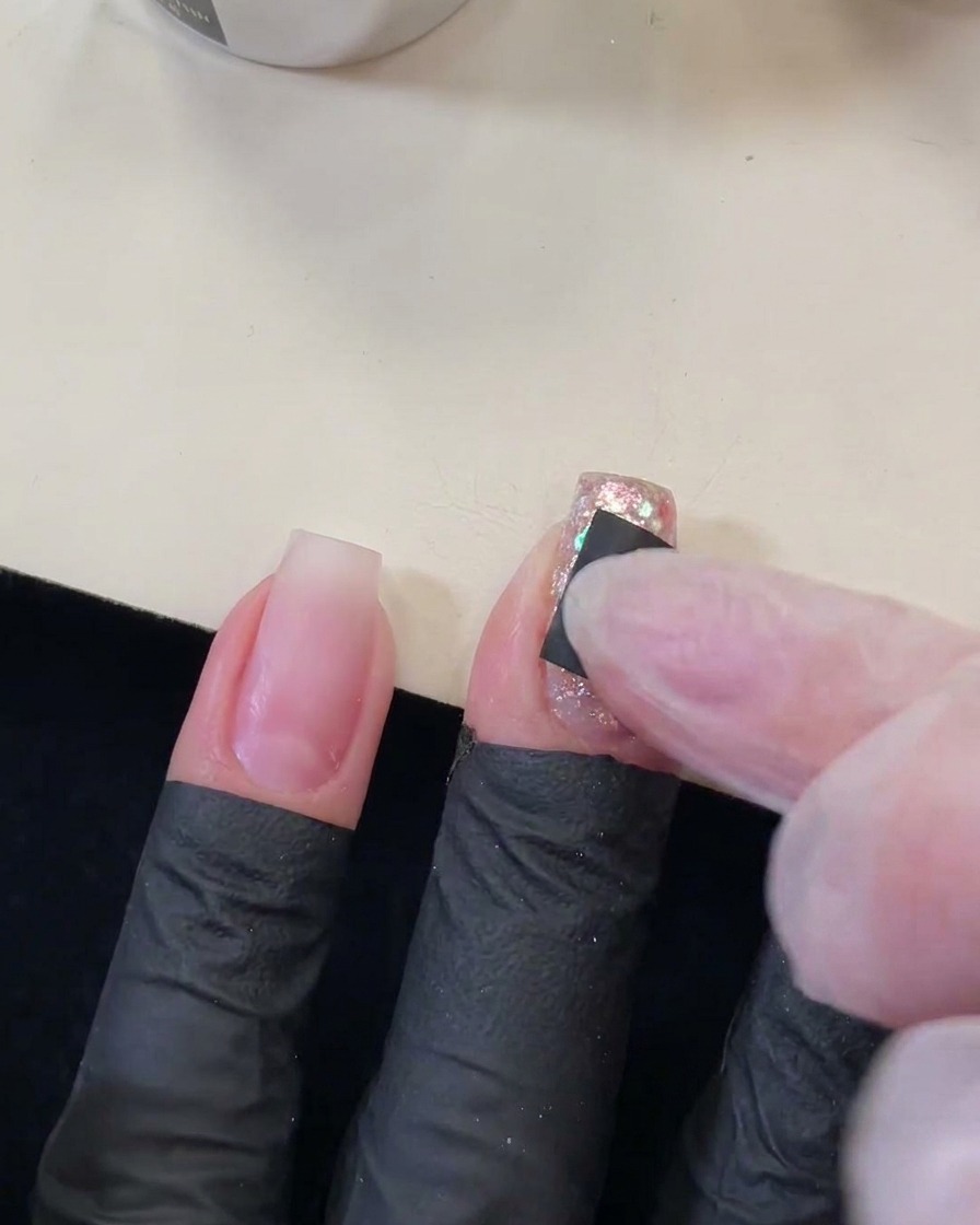Doigt pressant un petit autocollant carré noir avec une découpe en forme détoile sur un ongle scintillant et pailleté.