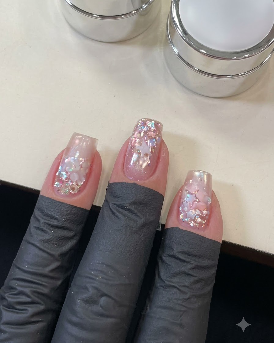 Gros plan dune main appliquant un top coat sur le nail art détaillé détoiles et de sequins.