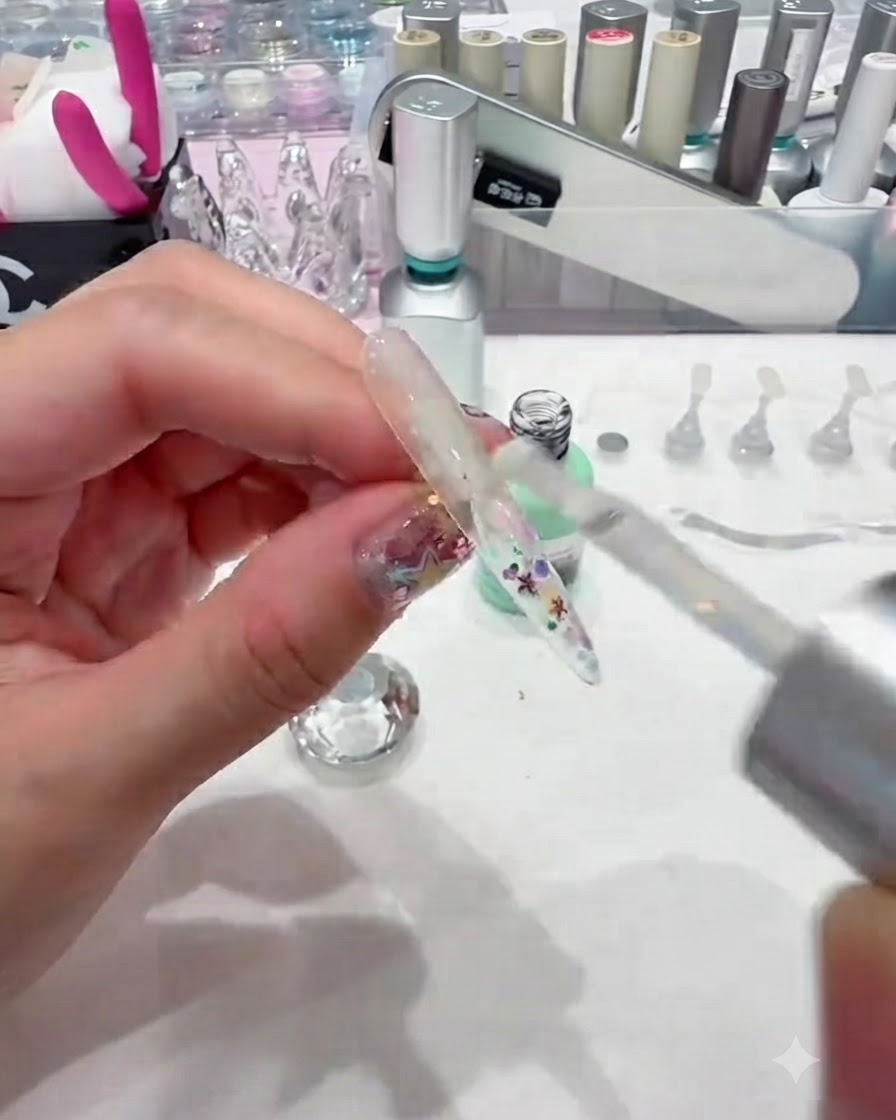 Un pinceau appliquant une couche épaisse de gel de construction transparent sur une capsule dongle pailletée pour lencapsuler en douceur.
