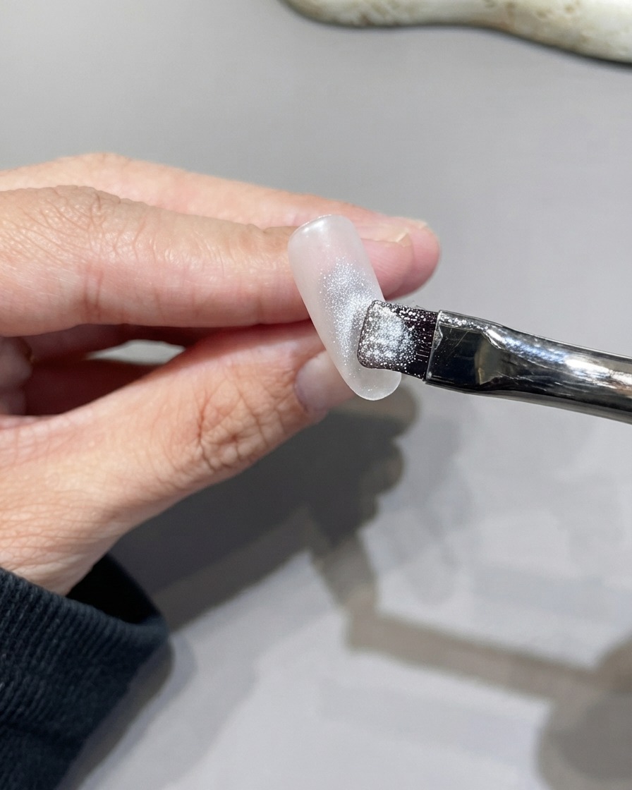 Un pinceau plat appliquant du gel œil de chat argenté et scintillant sur toute la surface dun ongle.