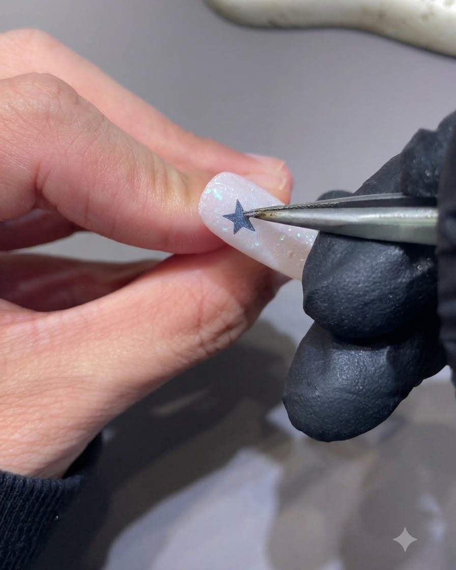 Une pince à épiler décollant un autocollant étoile dun ongle pour révéler une silhouette détoile évidée.