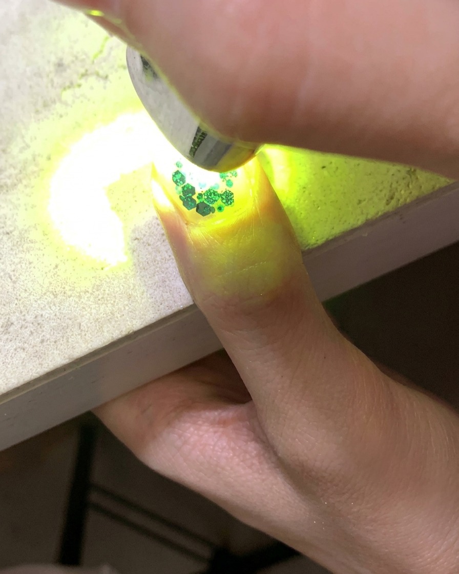 Une mini lampe UV catalysant un ongle orné de paillettes et de sequins étoiles creuses.