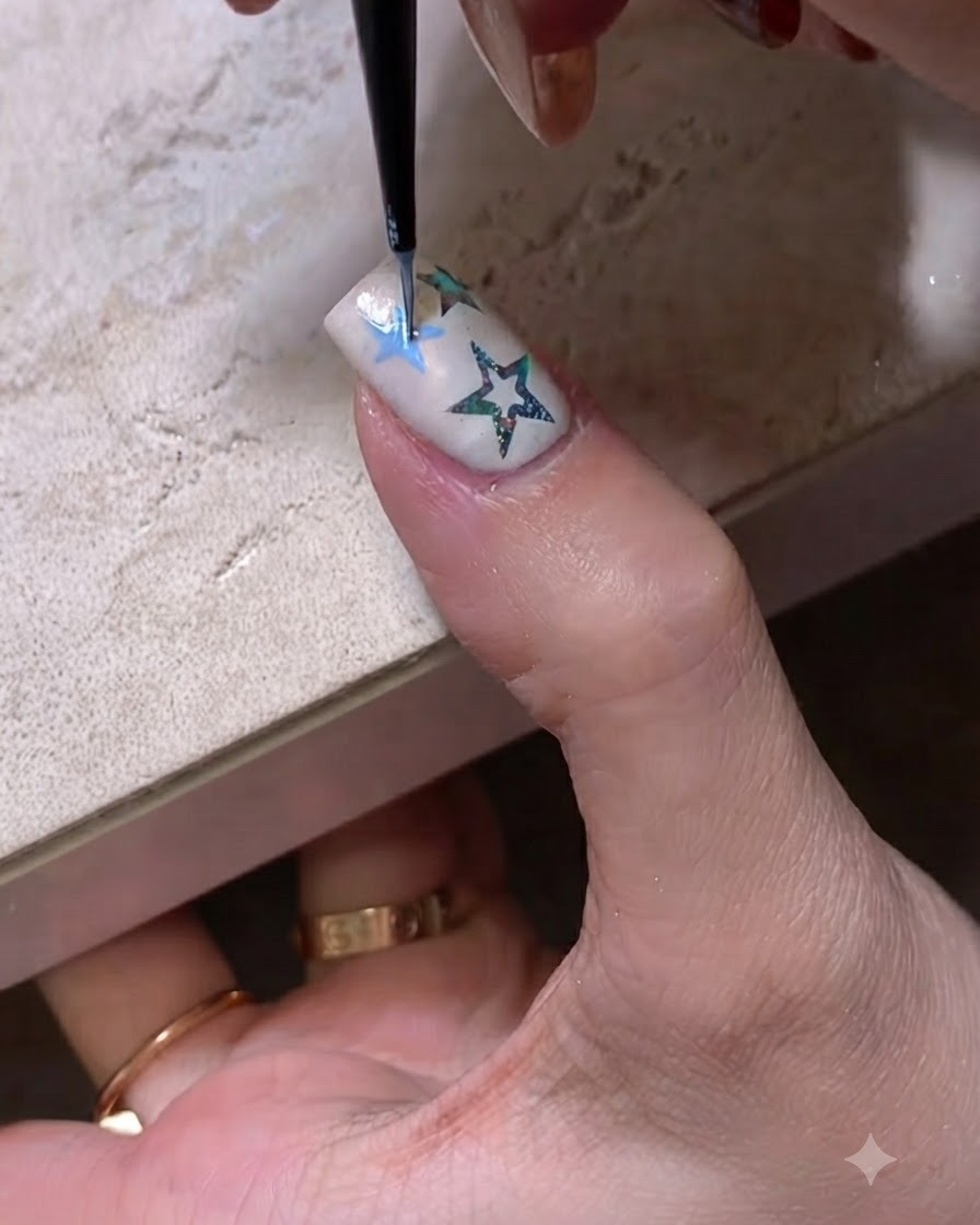 Gros plan dun pinceau fin de nail art dessinant un contour détoile bleu sur un ongle manucuré.