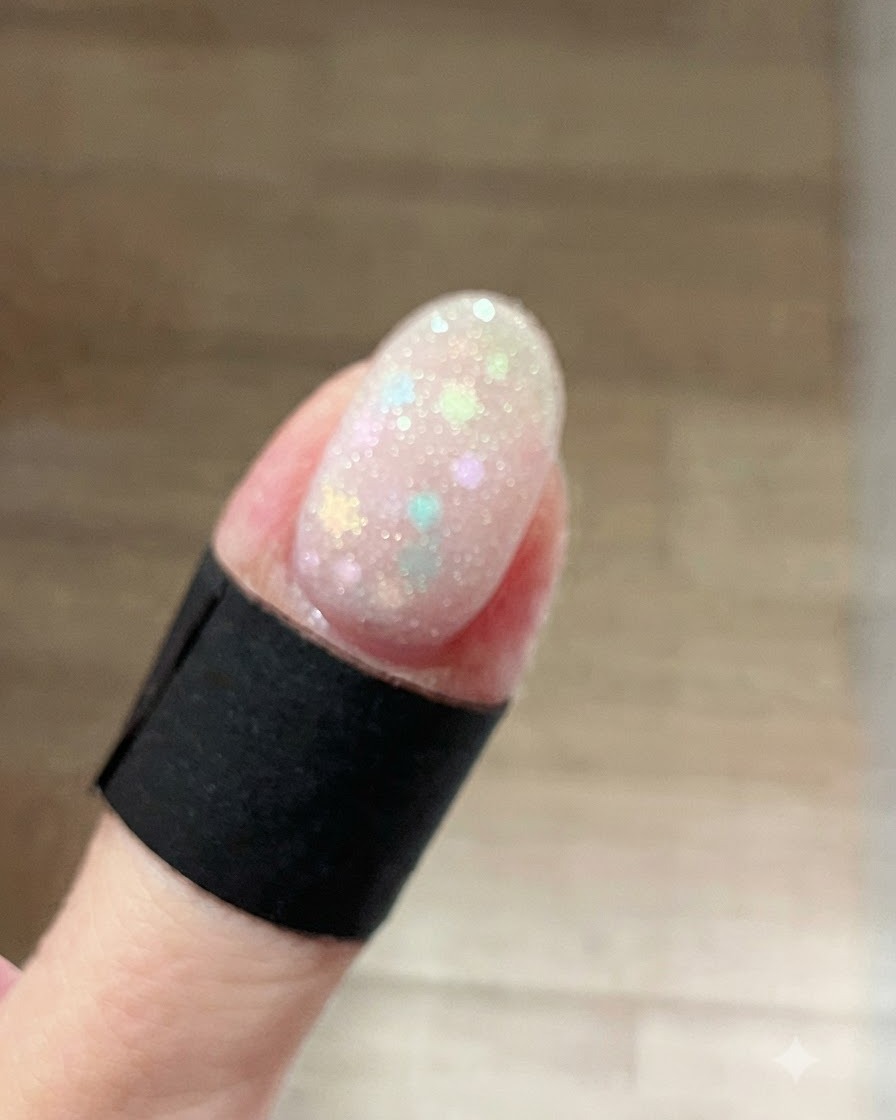 Gros plan sur un ongle recouvert dun gel scintillant blanc givré et humide superposé aux paillettes étoiles pastel.