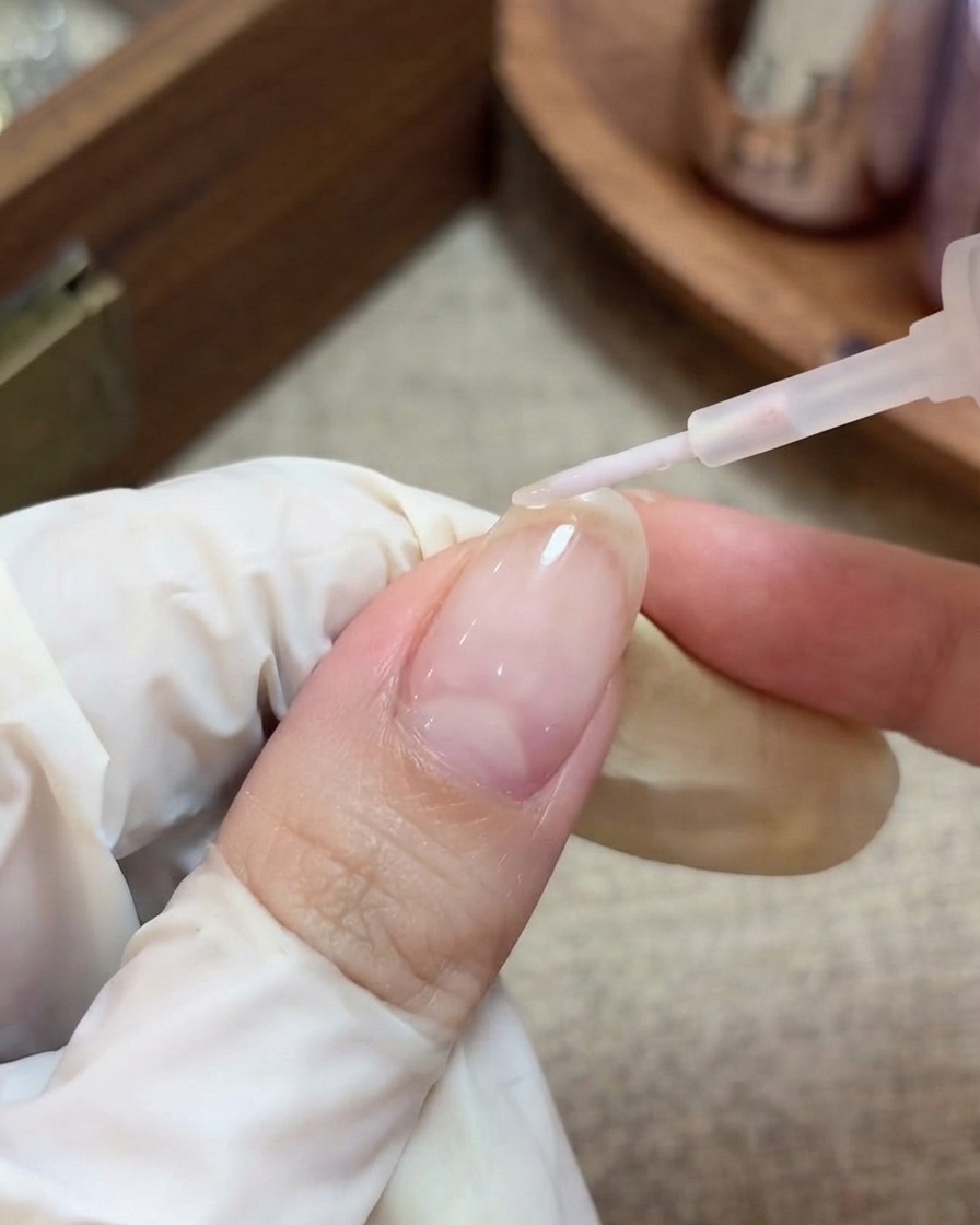 Une main gantée utilisant un pinceau pour appliquer un top coat transparent et brillant sur un ongle préparé avec des paillettes étoiles encapsulées.