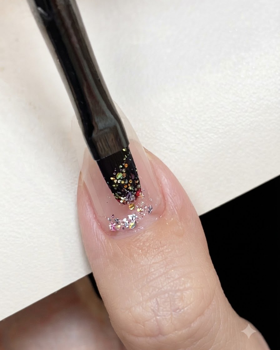 Un pinceau à gel plat appliquant du gel pailleté holographique rose au centre dun ongle préparé.