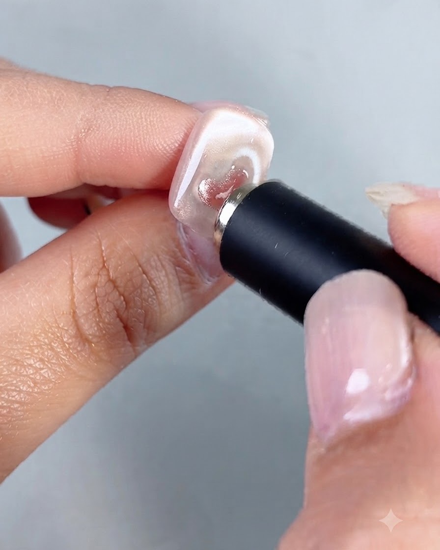 Un aimant cylindrique tenu près dun ongle, concentrant les reflets à lintérieur dun petit cœur cat-eye peint.