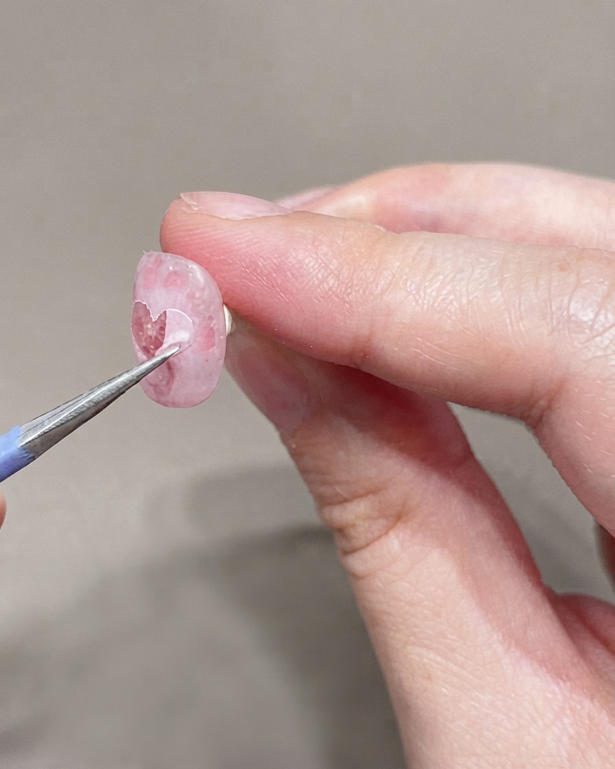 Un pinceau fin appliquant une deuxième couche de vernis gel rose très clair sur longle préparé.