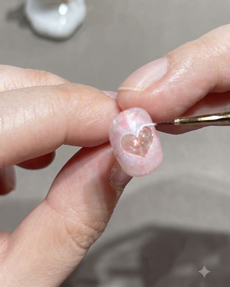 Un pinceau liner fin traçant le bord extérieur dun autocollant cœur sur un ongle en gel rose.